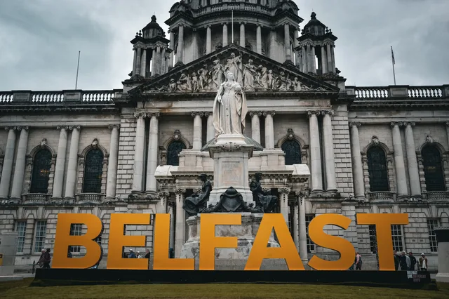 View of the Belfast City Hall with striking statue and Belfast sign, showcasing historical architecture. Belfast media outlets compared with Dublin for cross-border PR